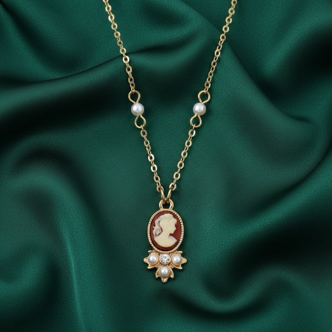 Gold necklace with a cameo pendant and faux pearls on the chain on a green fabric background