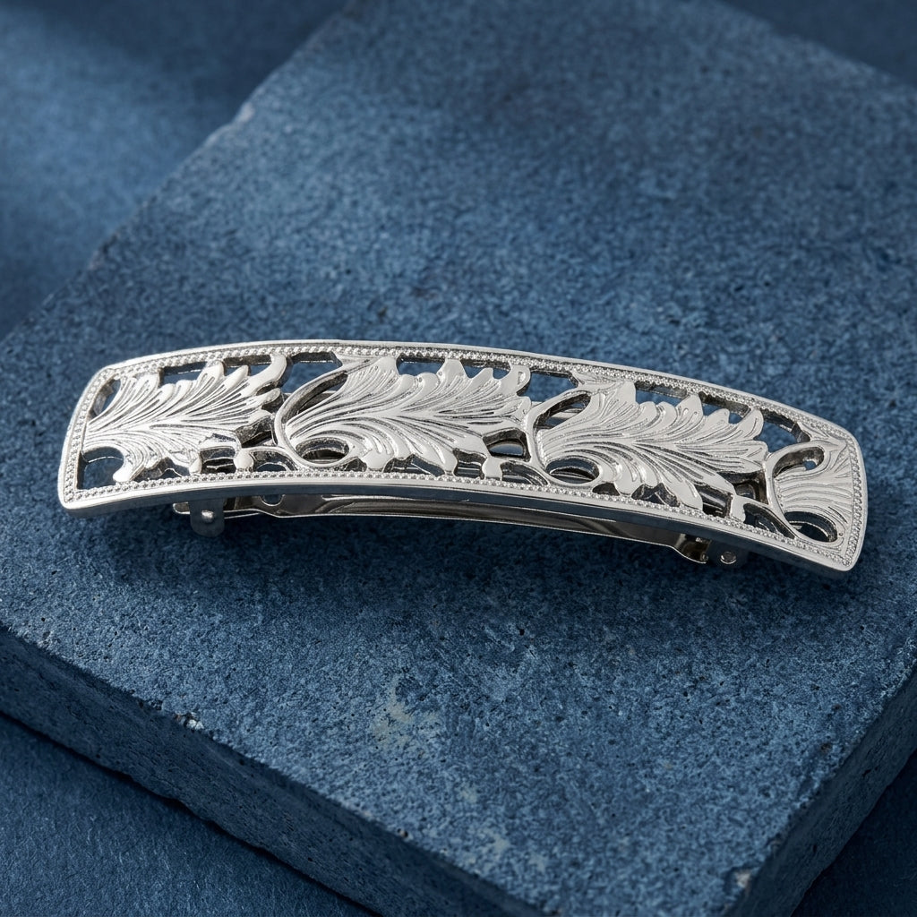 Silver hair clip with intricate leaf design on a blue textured background