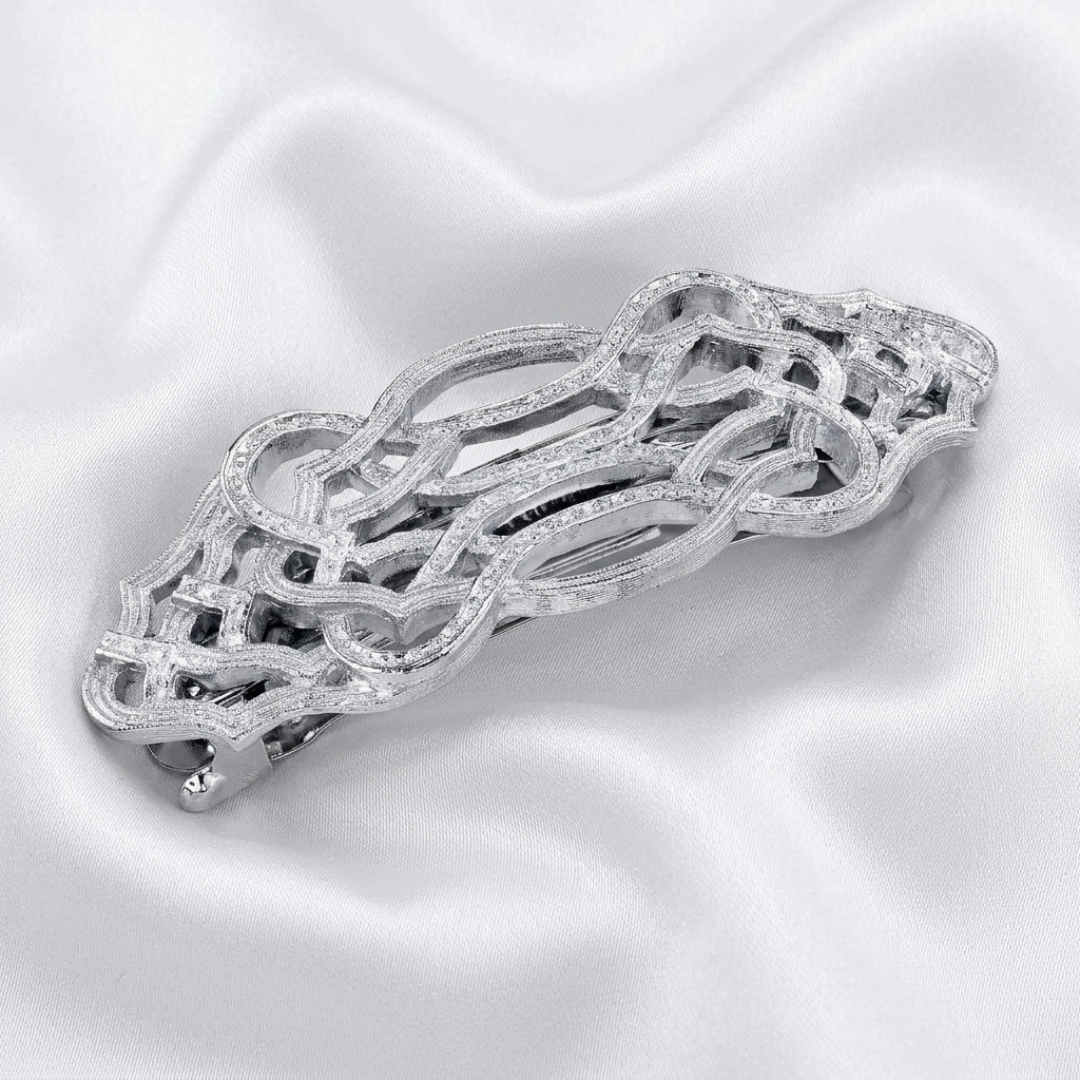 Silver barrette with intricate design on a white satin background