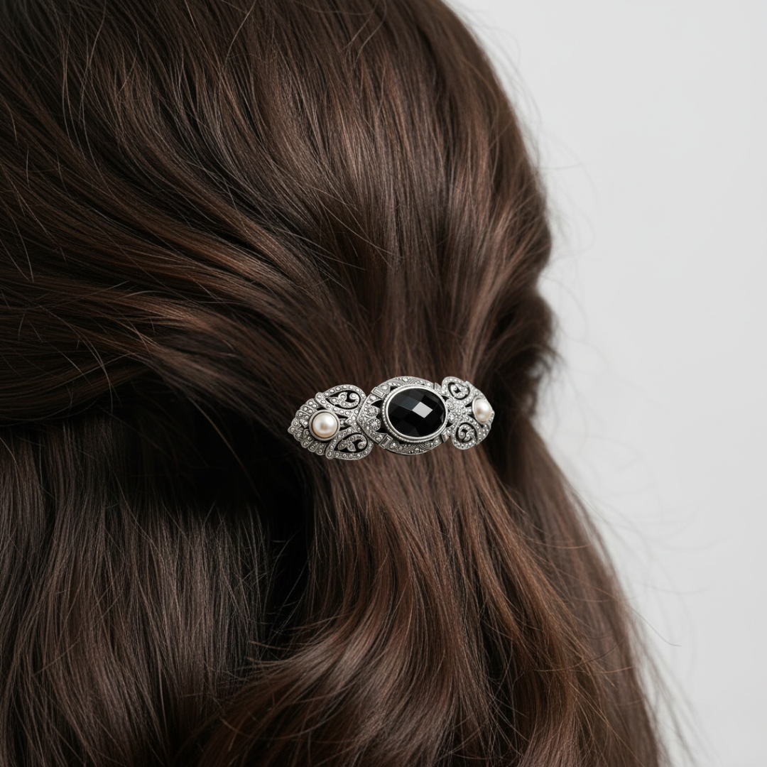 Silver hair barrette with a black gemstone and faux pearl on brown hair against a white background.