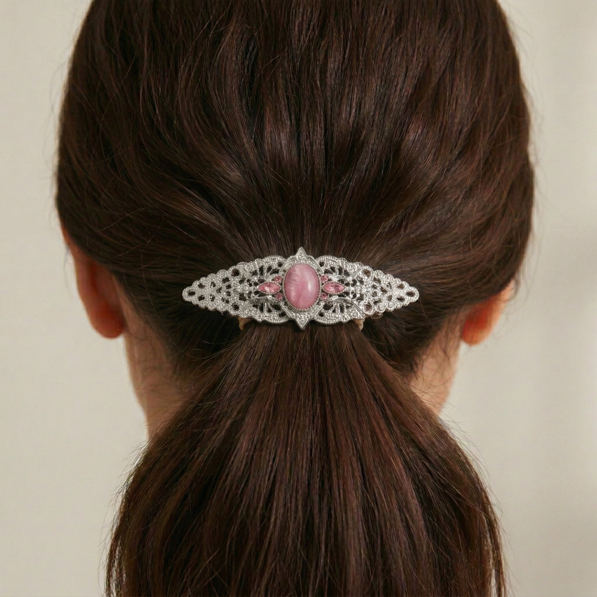 Hair barrette with a pink gemstone and lace design on a person's hair.