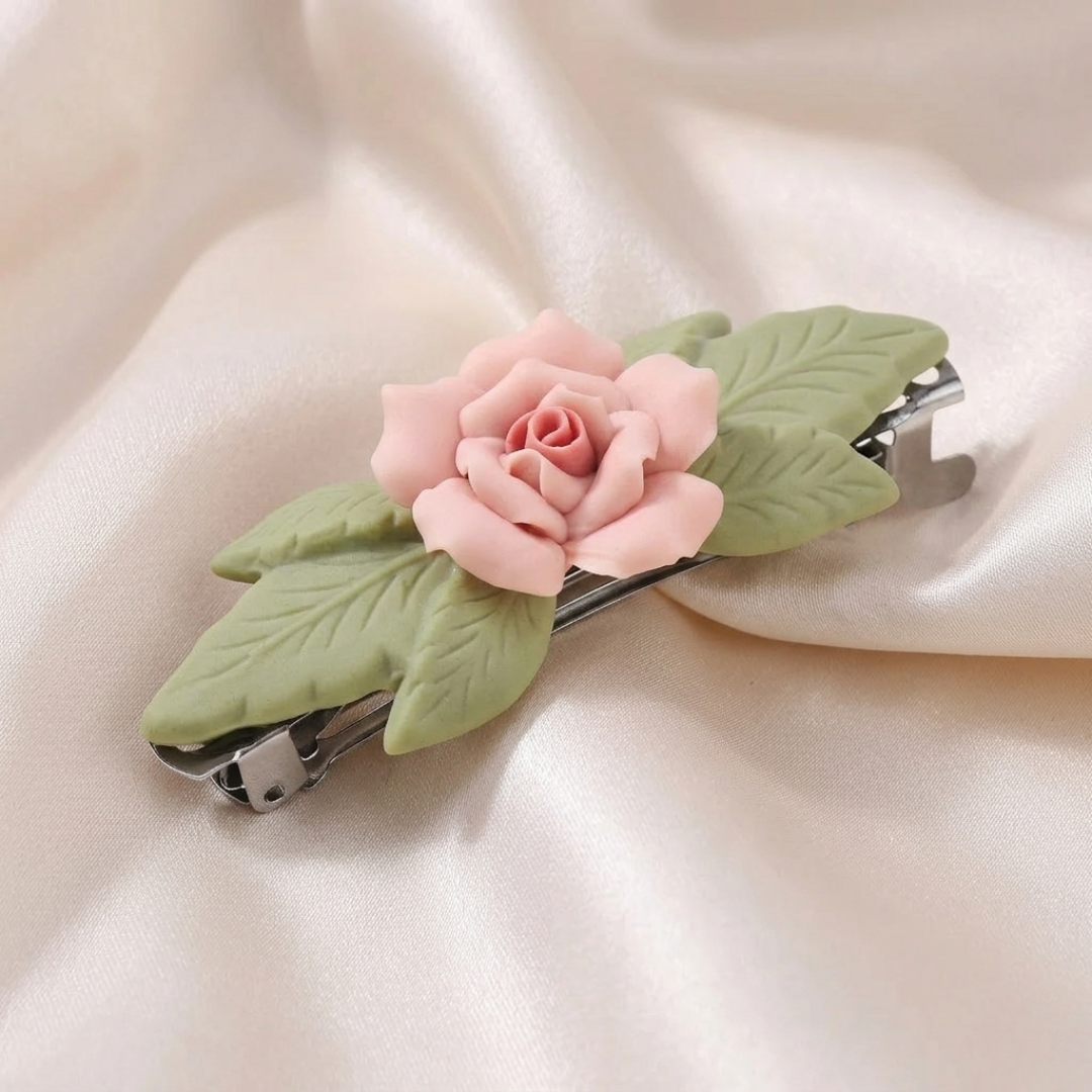 Hair clip with pink porcelain rose and green leaves on a beige fabric background