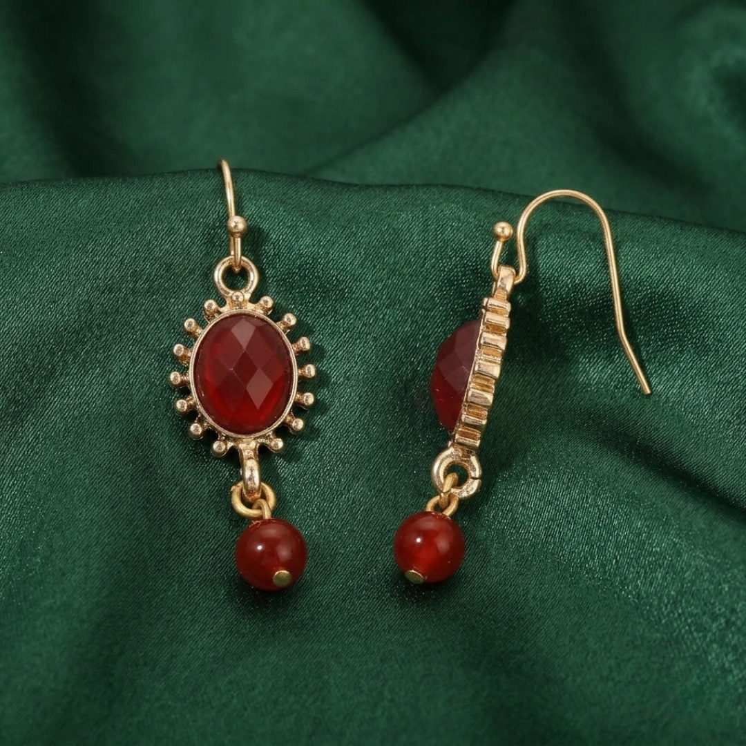 Gold earrings with red crystals on a green fabric background