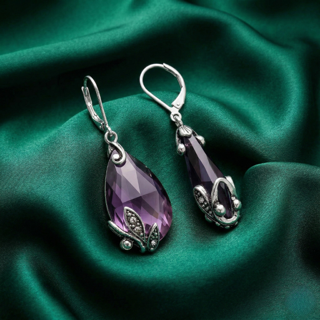 Purple teardrop earrings with silver accents on a green fabric background