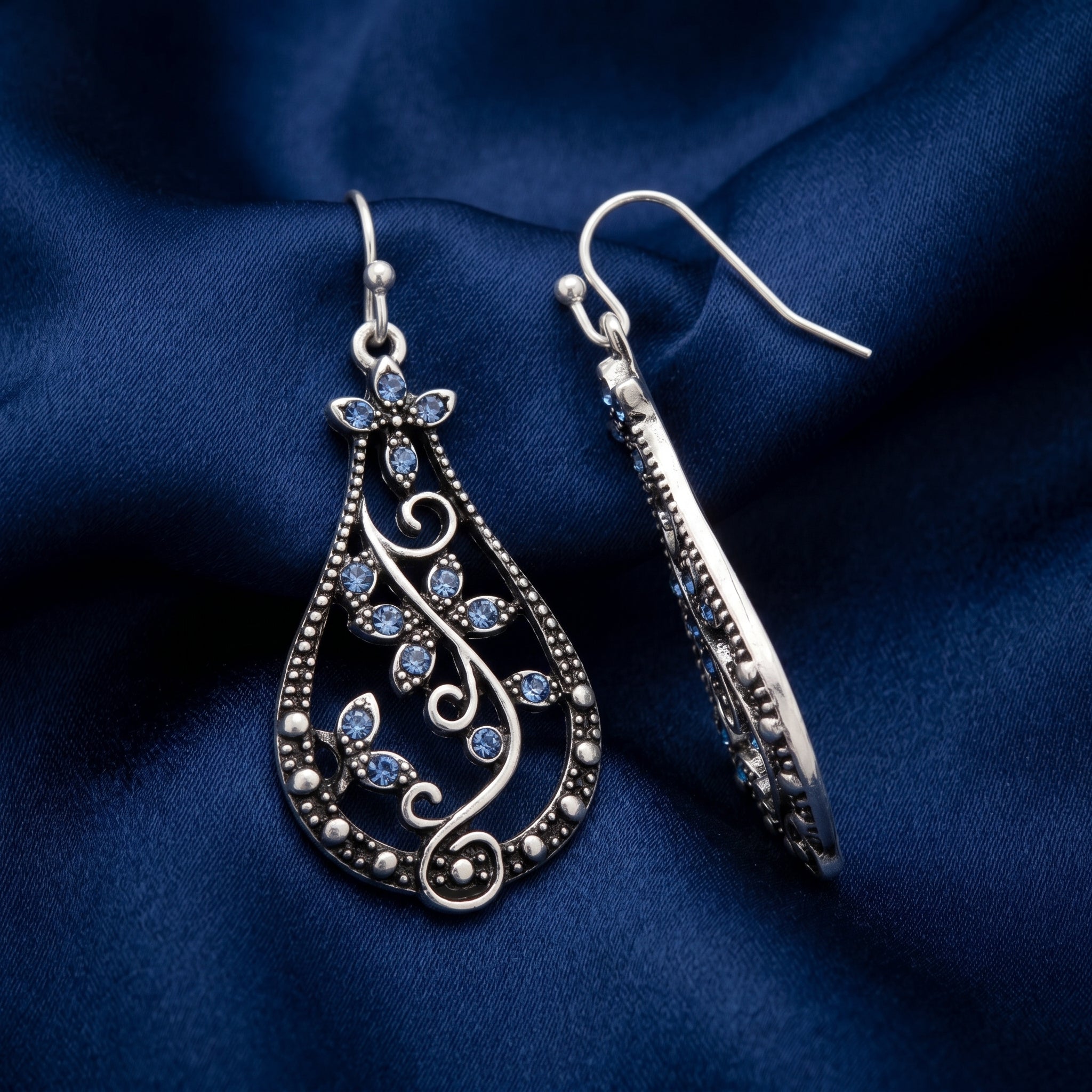 Teardrop Vine Light Sapphire Crystal Drop Earrings on a blue fabric background