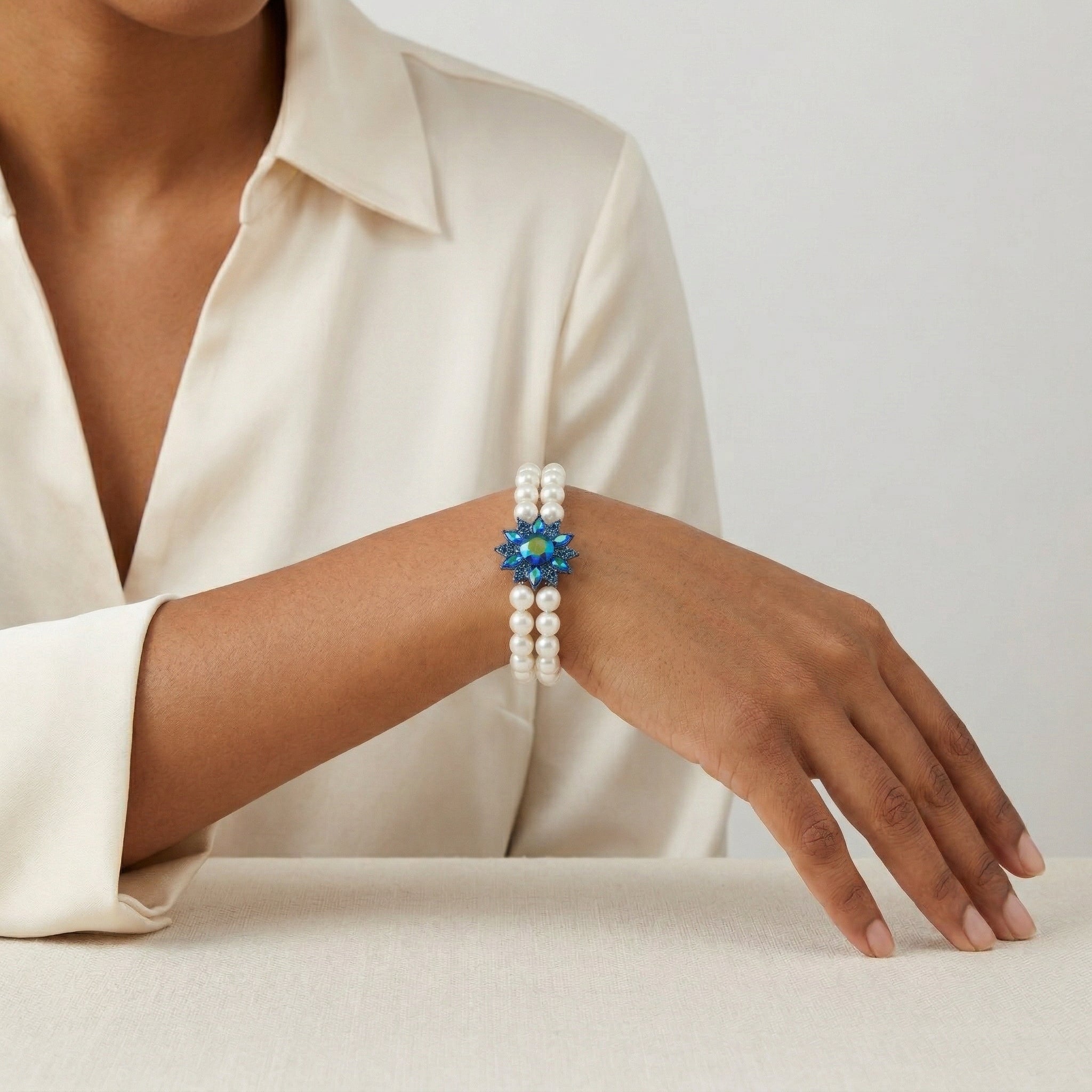 Pearl bracelet with a blue AB crystal floral center worn by a person in a cream shirt.
