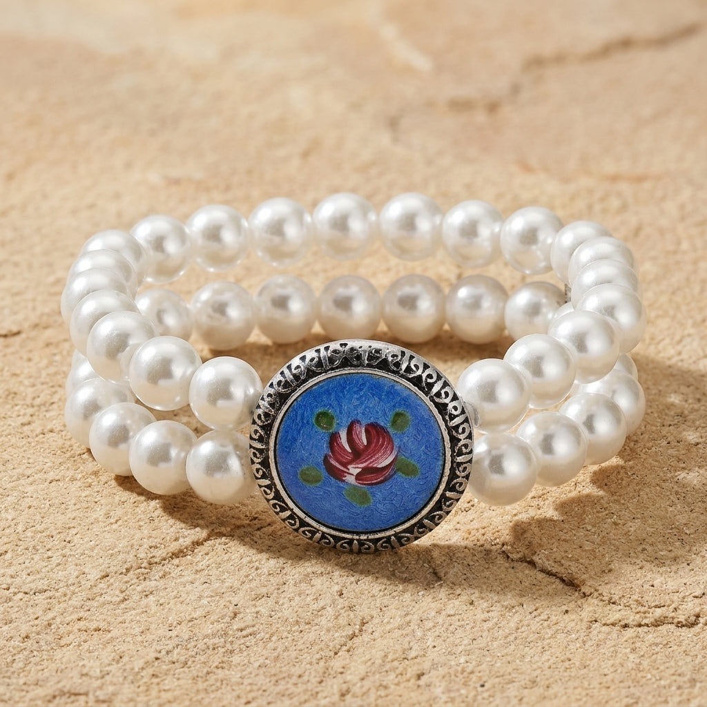 Silver Tone Blue & Pink Flower Decal Double Strand Pearl Bead Stretch Bracelet on a sandy stone background