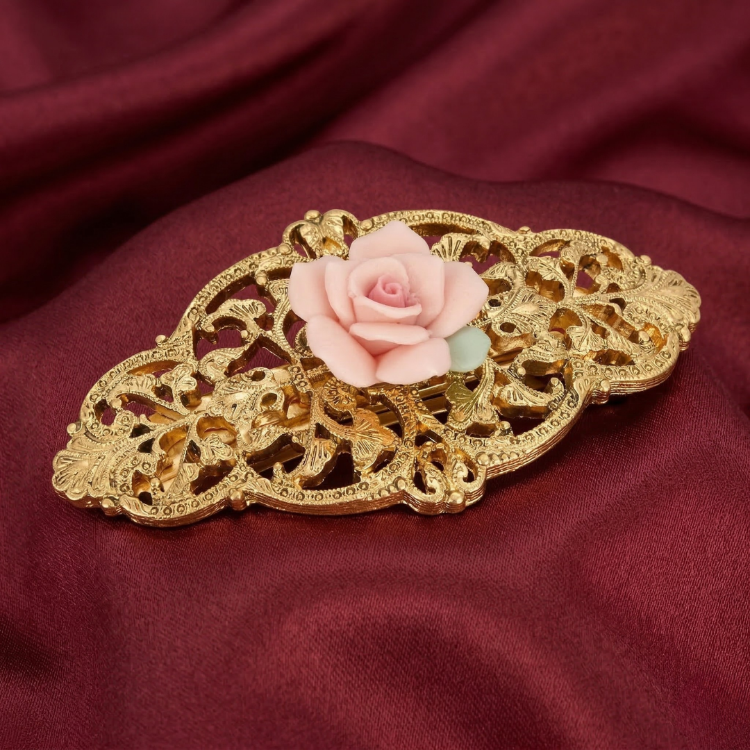 Decorative barrette with pink porcelain rose on a gold filigree setting against a red fabric background