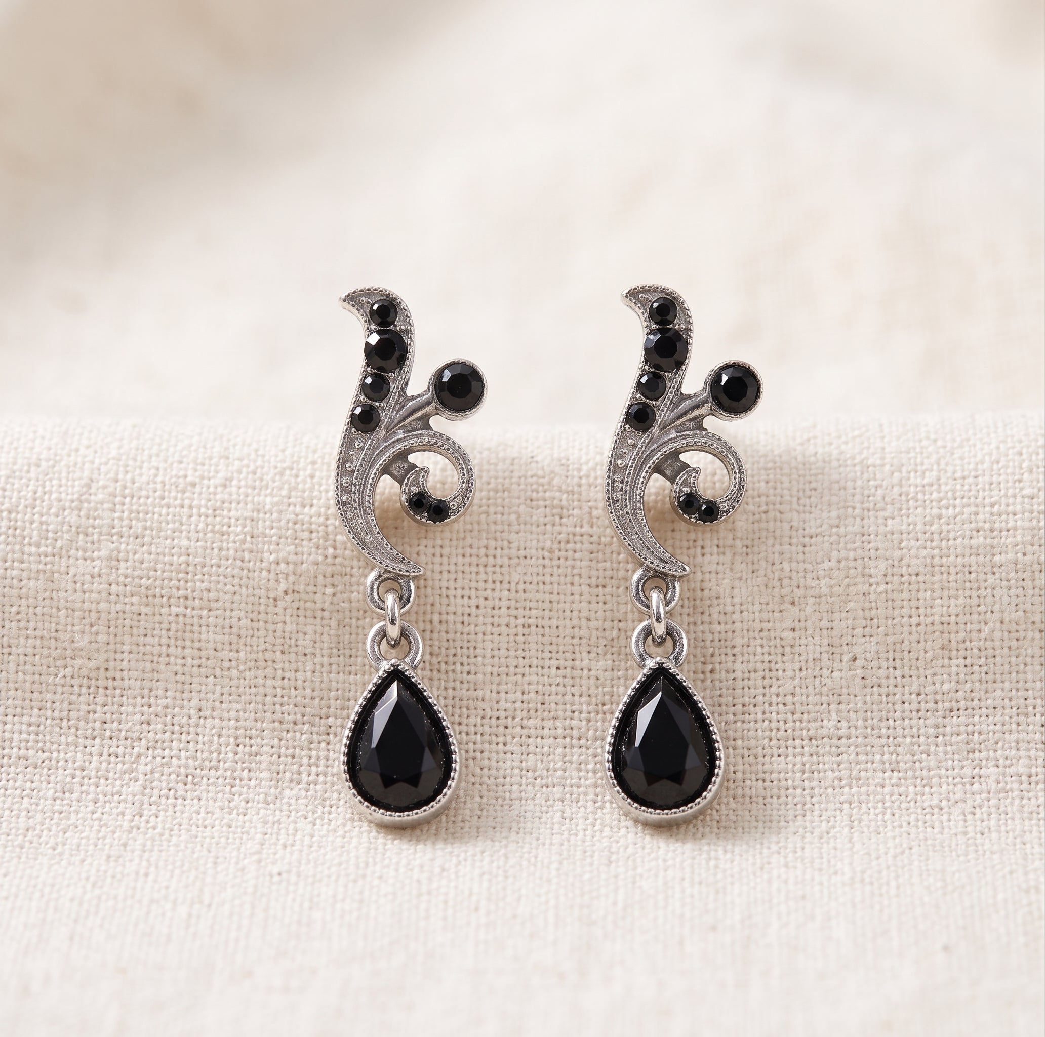 Antiquities Couture Black And Hematite Color Crystal Vine Drop Earrings on a beige linen background