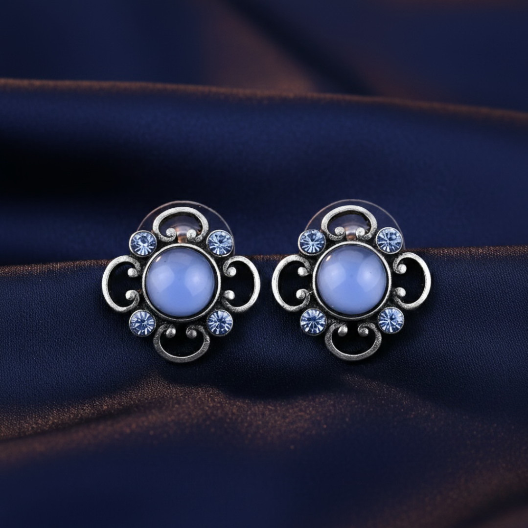Pair of decorative earrings with blue gemstones on a dark fabric background