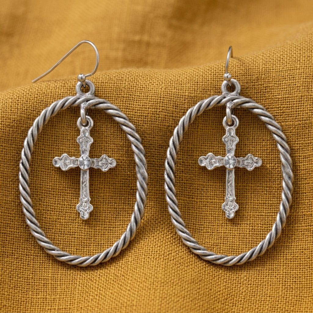 Silver Crystal Accent Suspended Cross Drop Hoop Earrings displayed on a textured mustard yellow fabric background.