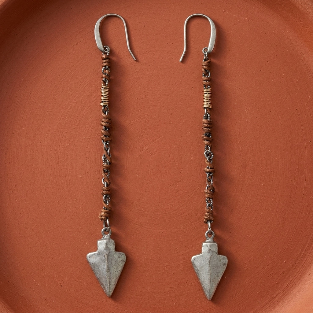 Walnut Brown Wrapped Linear Arrowhead Earrings resting on a smooth red clay surface
