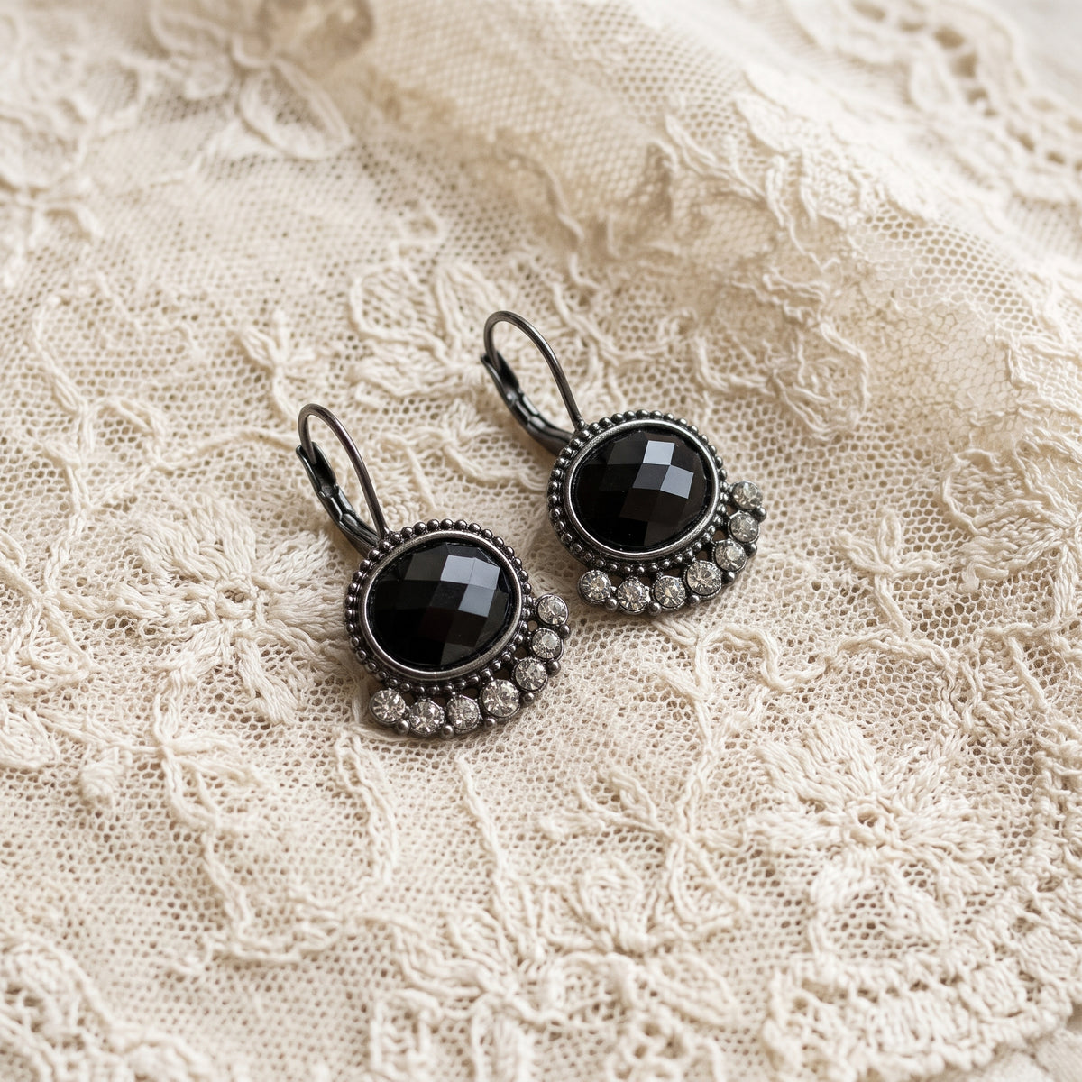 Black Oval Stone & Diamond Crystal Lever Back Earrings resting on a textured cream lace fabric.