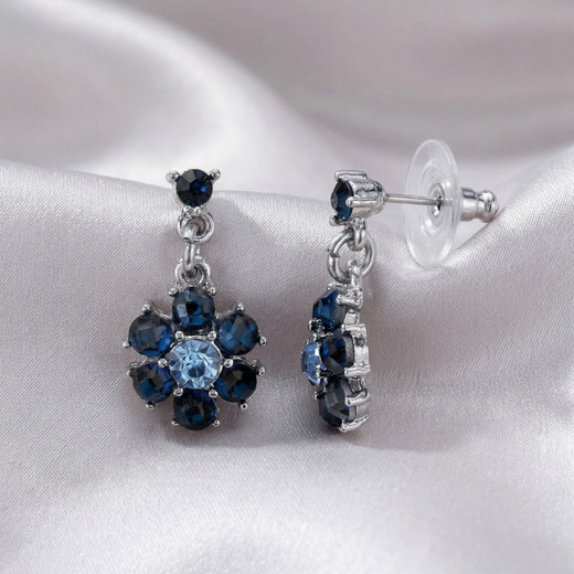Pair of silver floral-shaped earrings with blue crystals on a white satin background