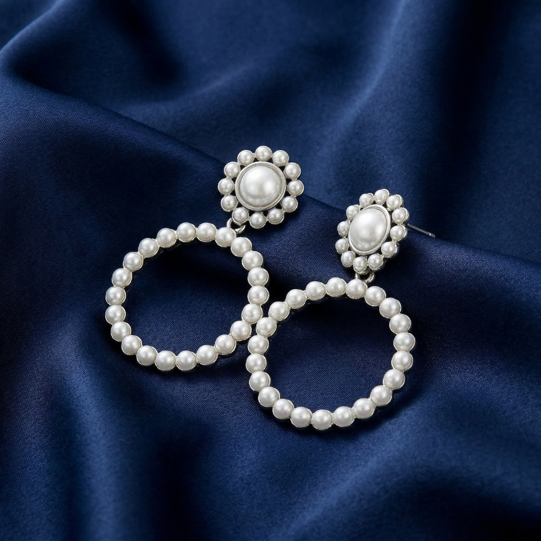 Faux pearl hoop earrings on a dark blue fabric background