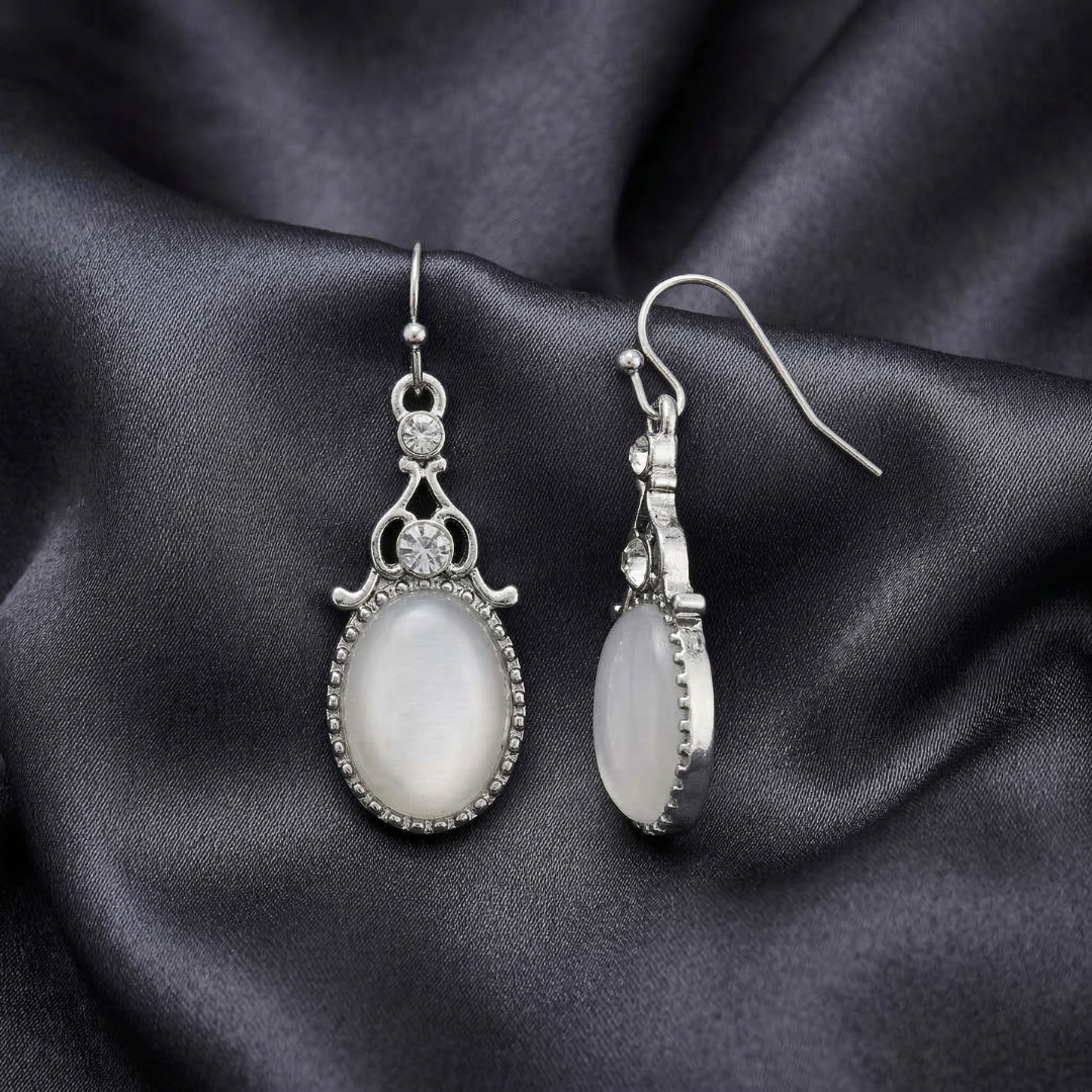 Pair of silver earrings with white stones on a dark fabric background