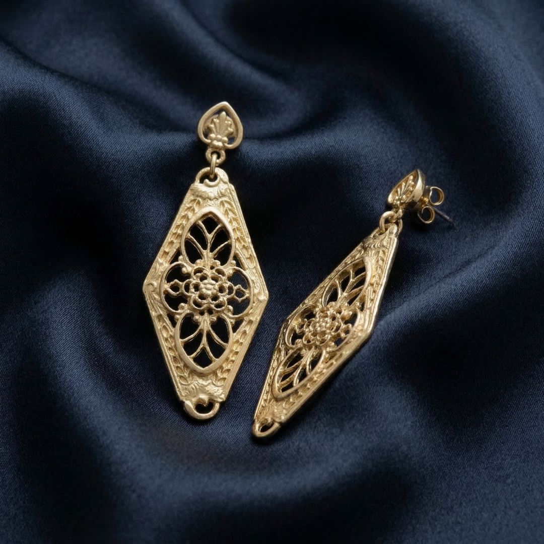 Gold filigree earrings shaped like lanterns on a dark blue fabric background