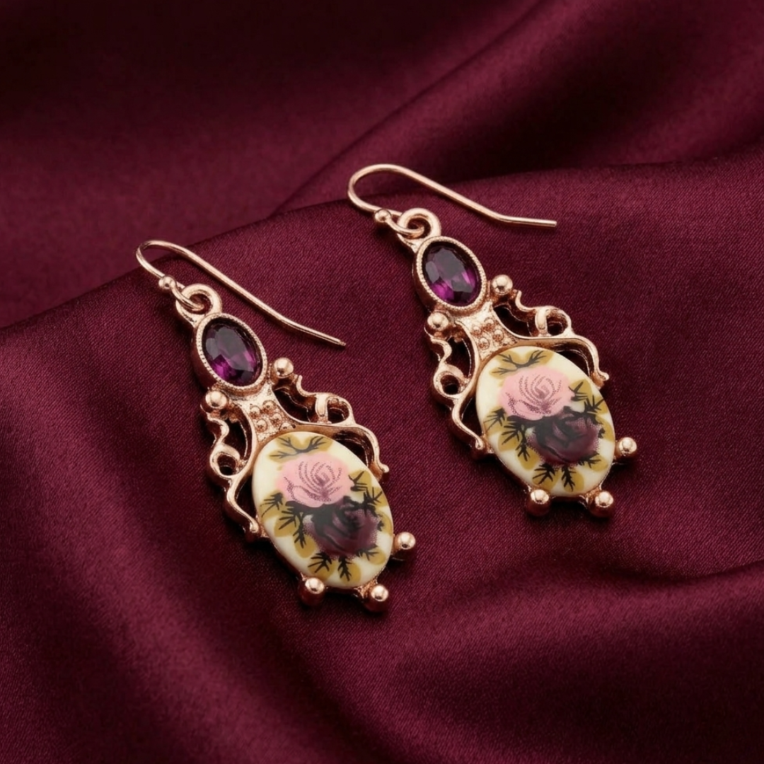 Ornate earrings with floral designs on a maroon fabric background