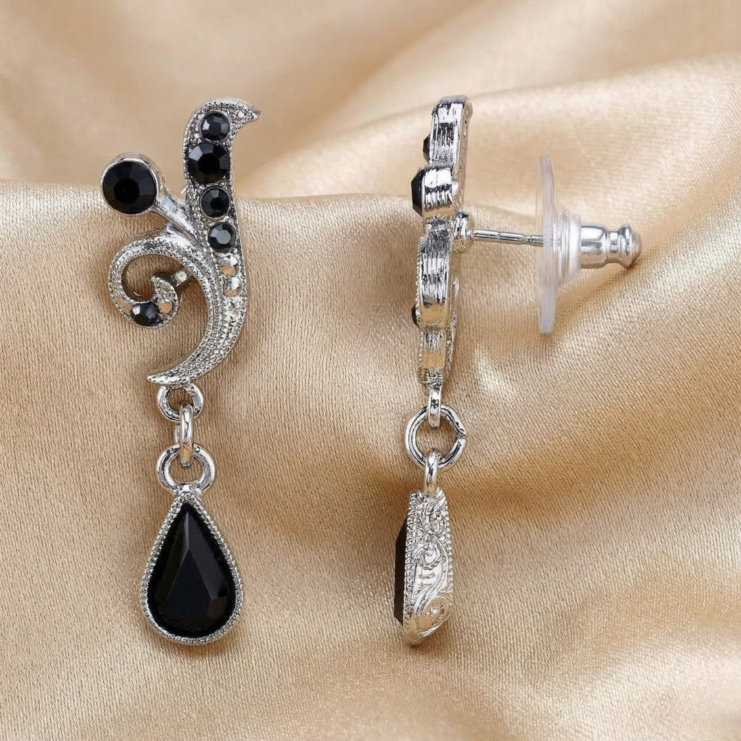 Silver earrings with black teardrop crystals on a beige satin background
