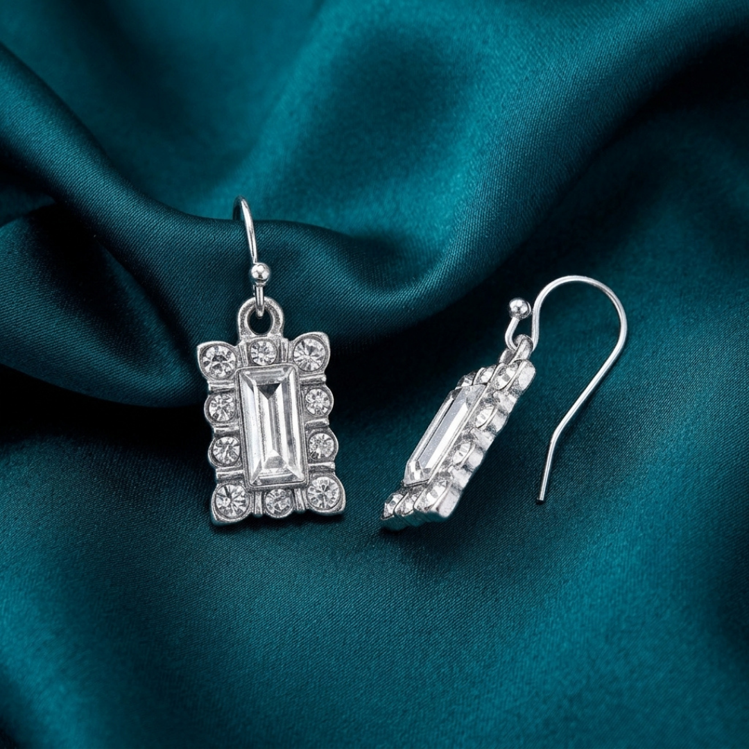 Silver earrings with clear crystals on a teal fabric background