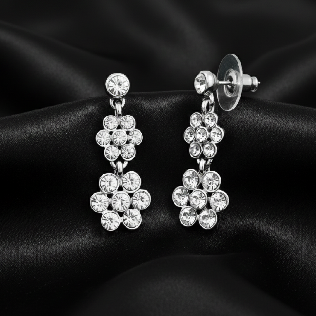 Silver crystal dangle earrings on a black satin fabric.