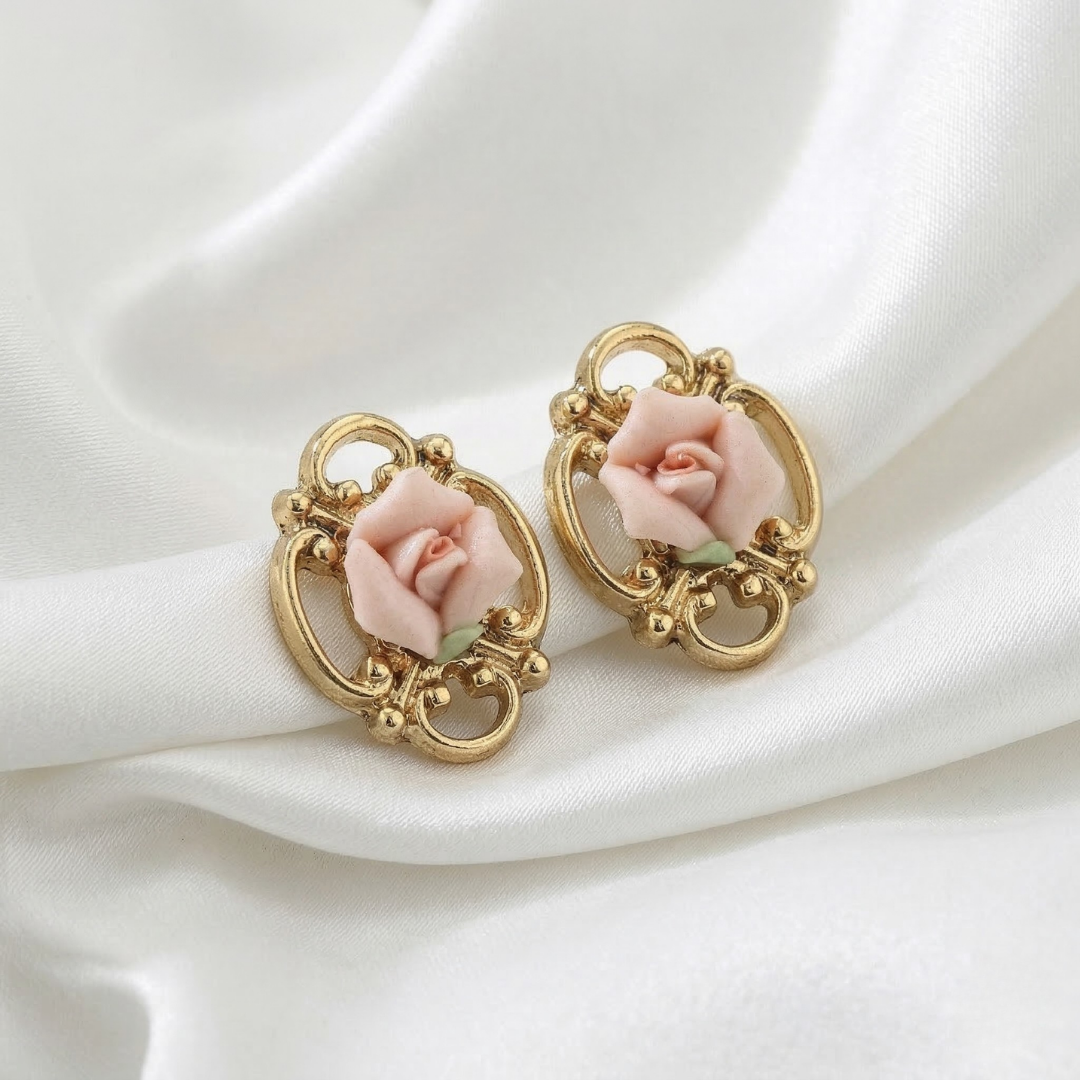 Gold earrings with pink porcelain rose details on a white fabric background