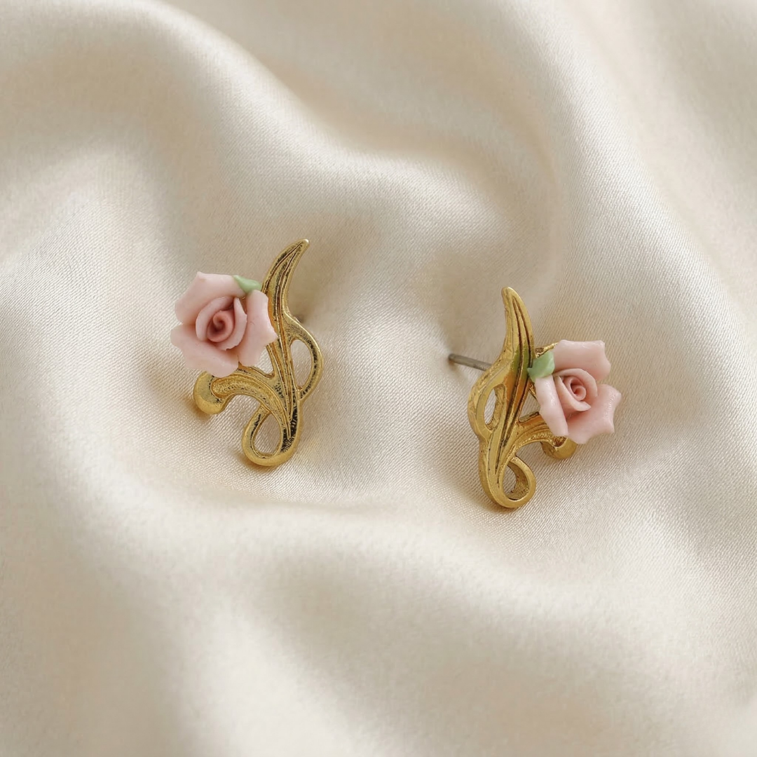 Gold earrings with pink porcelain rose details on a beige fabric background