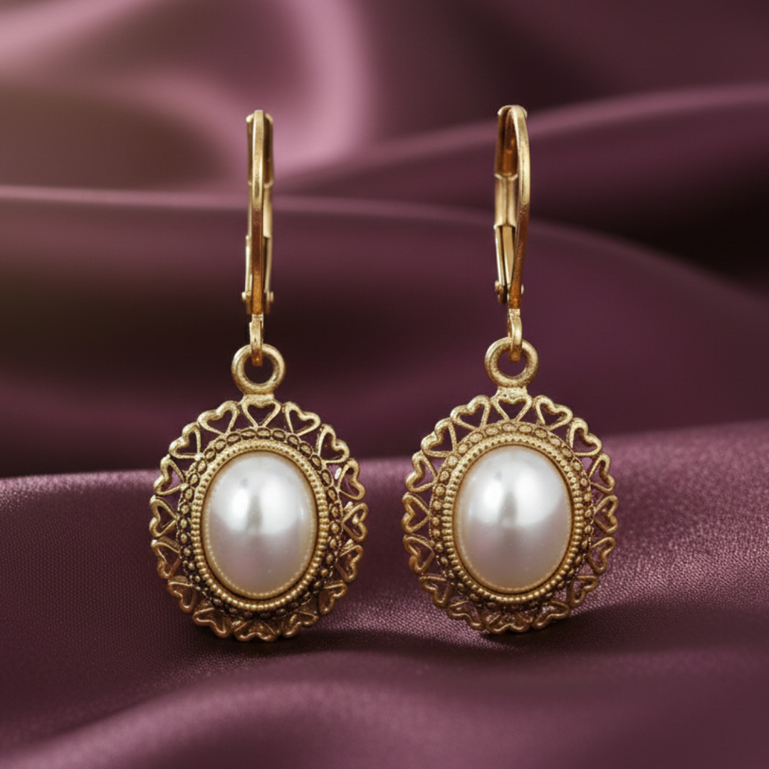 Gold earrings with faux pearl stones on a purple fabric background.