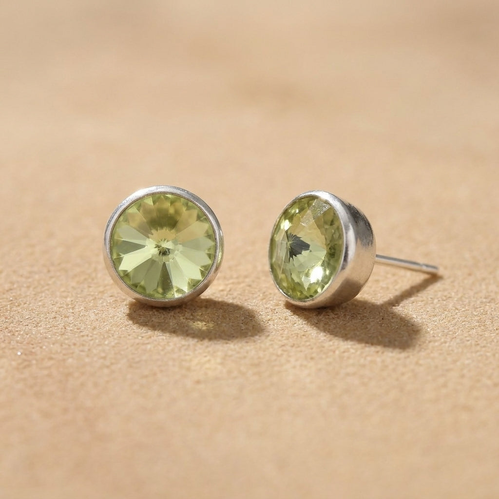 Petite Light Green Austrian Crystal Stud Earrings resting on smooth sand surface