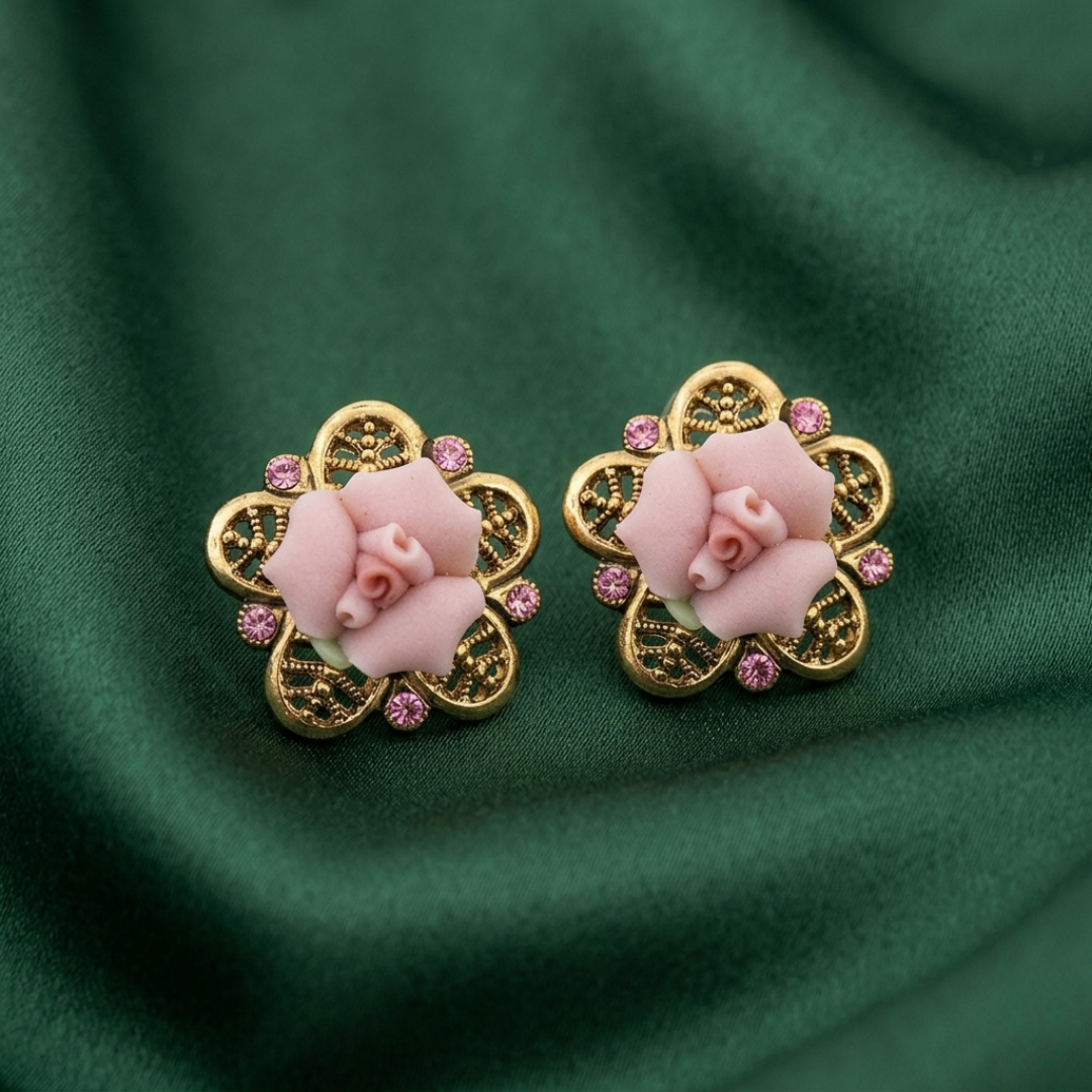 Pair of gold earrings with pink floral designs on a green fabric background
