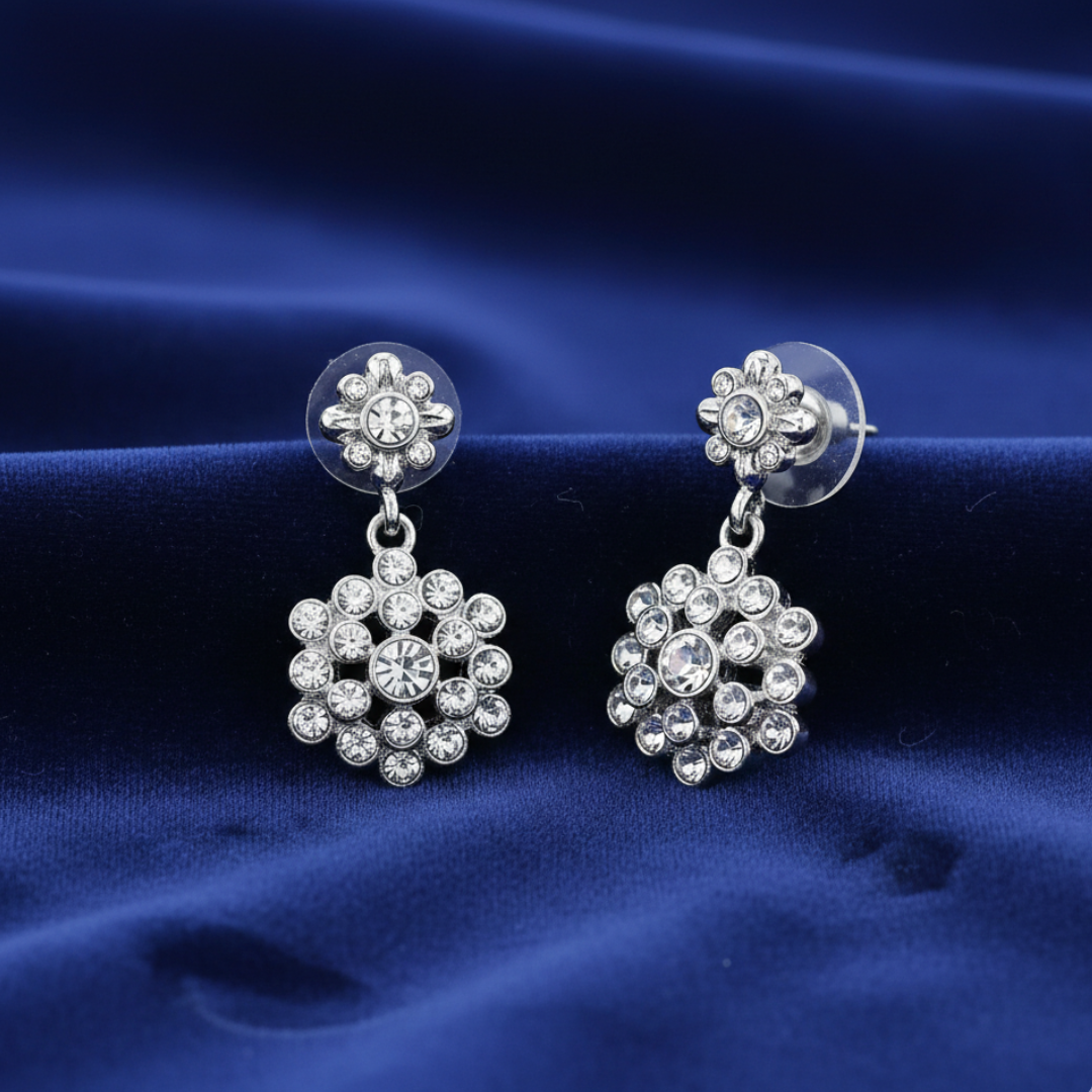 Silver earrings with clear crystals on a blue fabric background