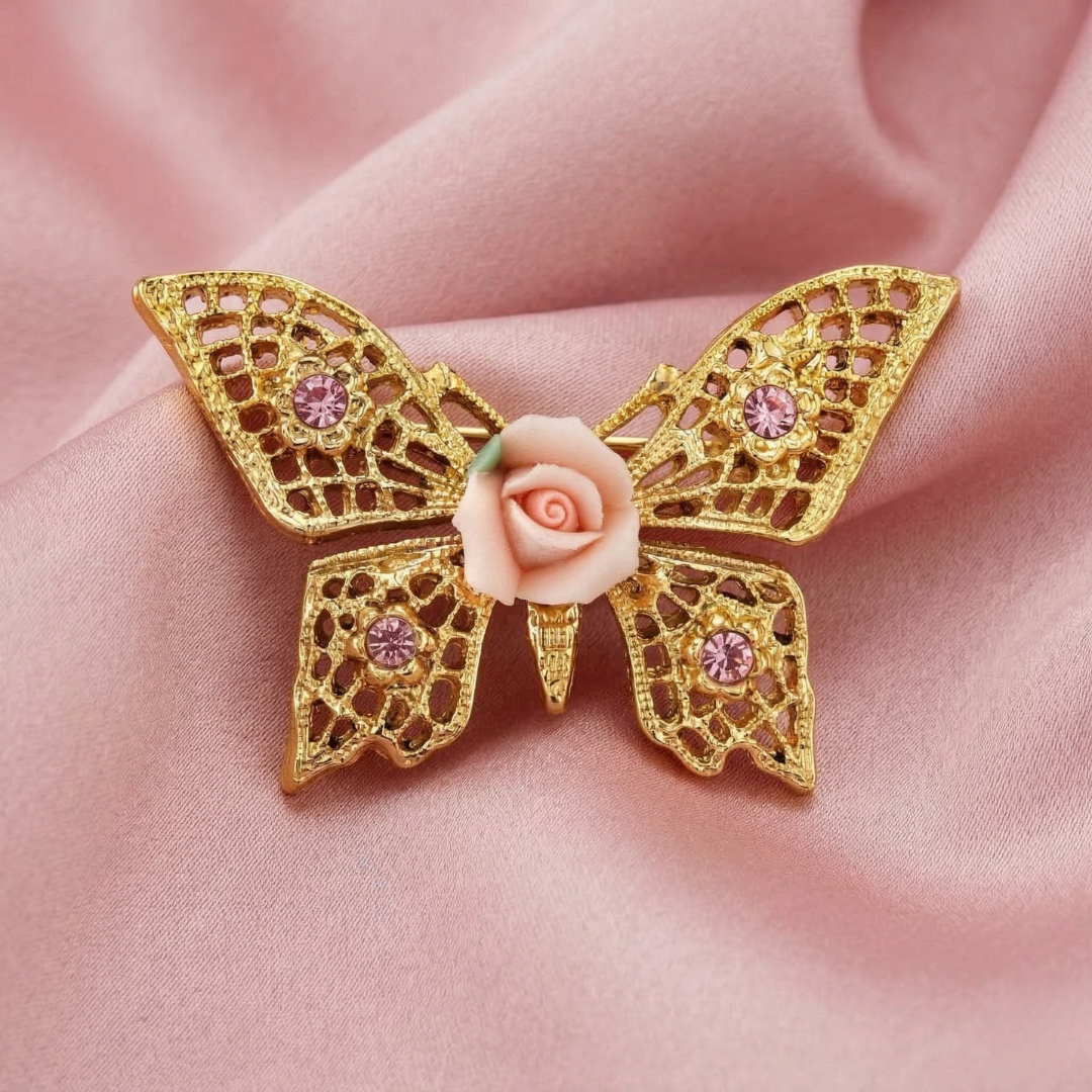 Gold butterfly brooch with pink crystals and a pink porcelain rose on a pink fabric background