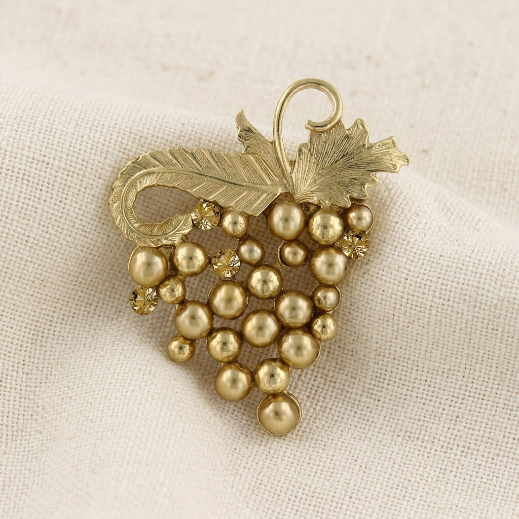 Gold tone faux pearl wine grape brooch pin resting on white linen