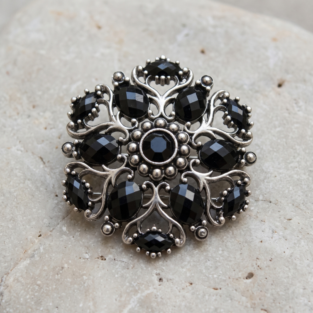 Jet Black Stone Ornate Brooch Pin displayed on a textured light beige stone surface.