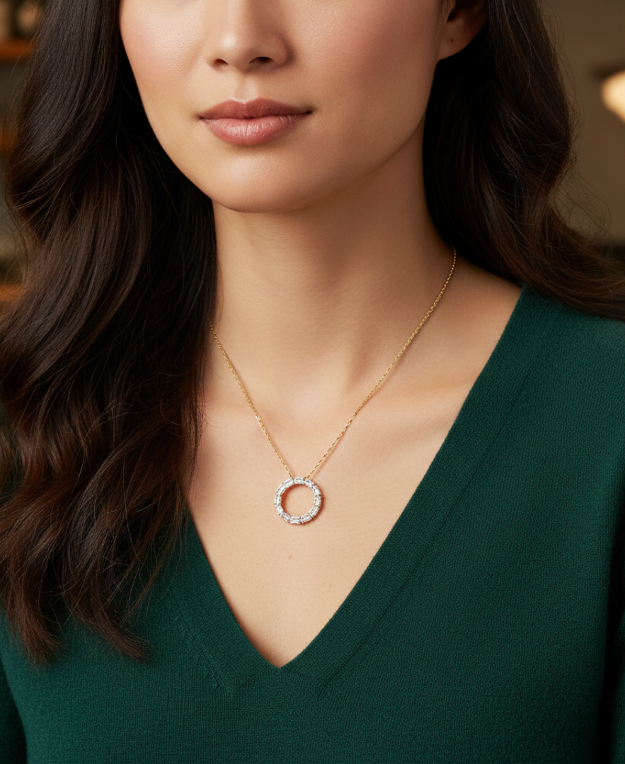 Woman wearing a gold necklace with a circular pendant against a blurred indoor background.