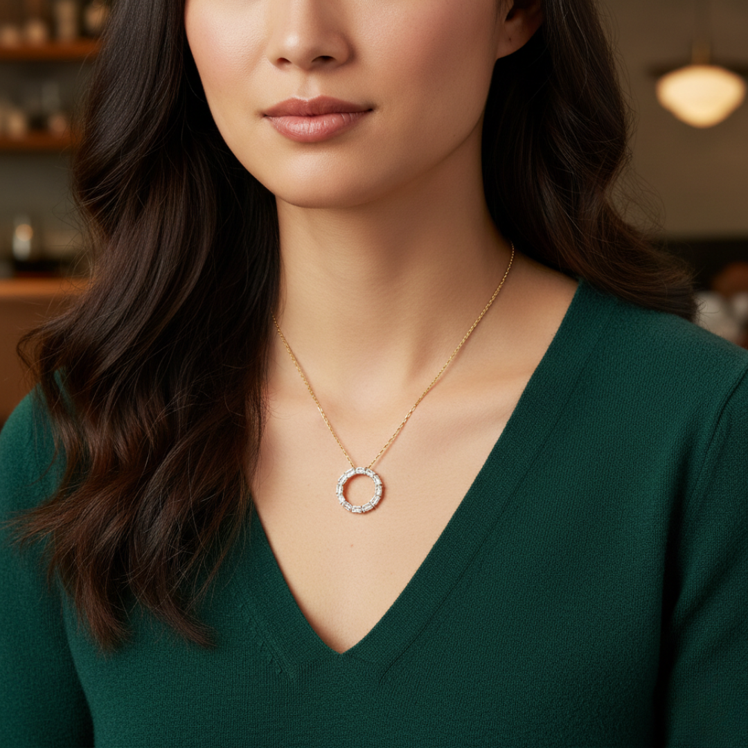 Woman wearing a gold necklace with a circular pendant against a blurred indoor background.