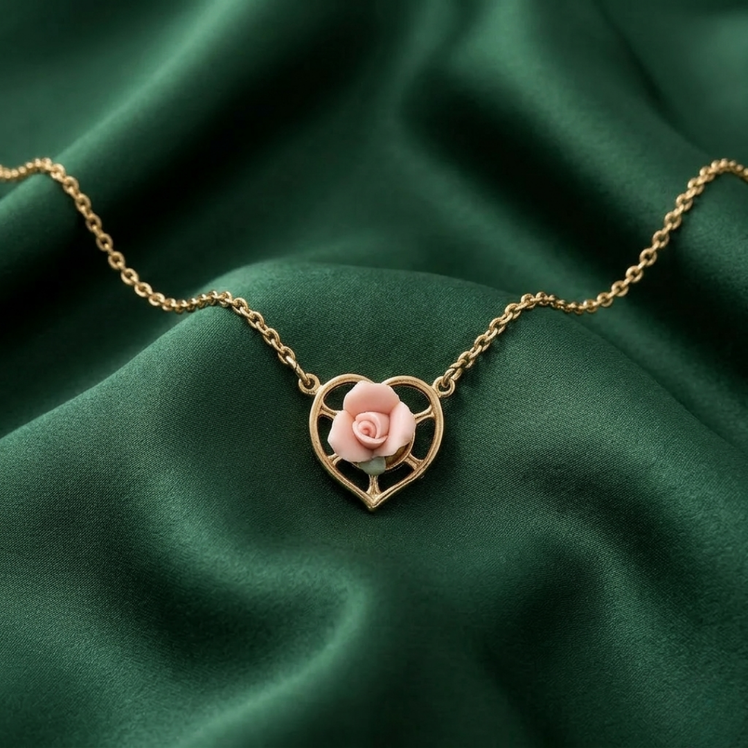 Gold necklace with a heart-shaped pendant featuring a pink rose on a green fabric background