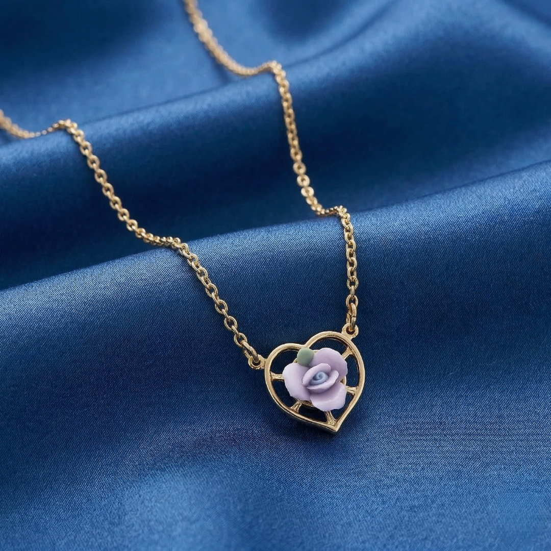 Gold necklace with a heart-shaped pendant featuring a purple rose on a blue fabric background