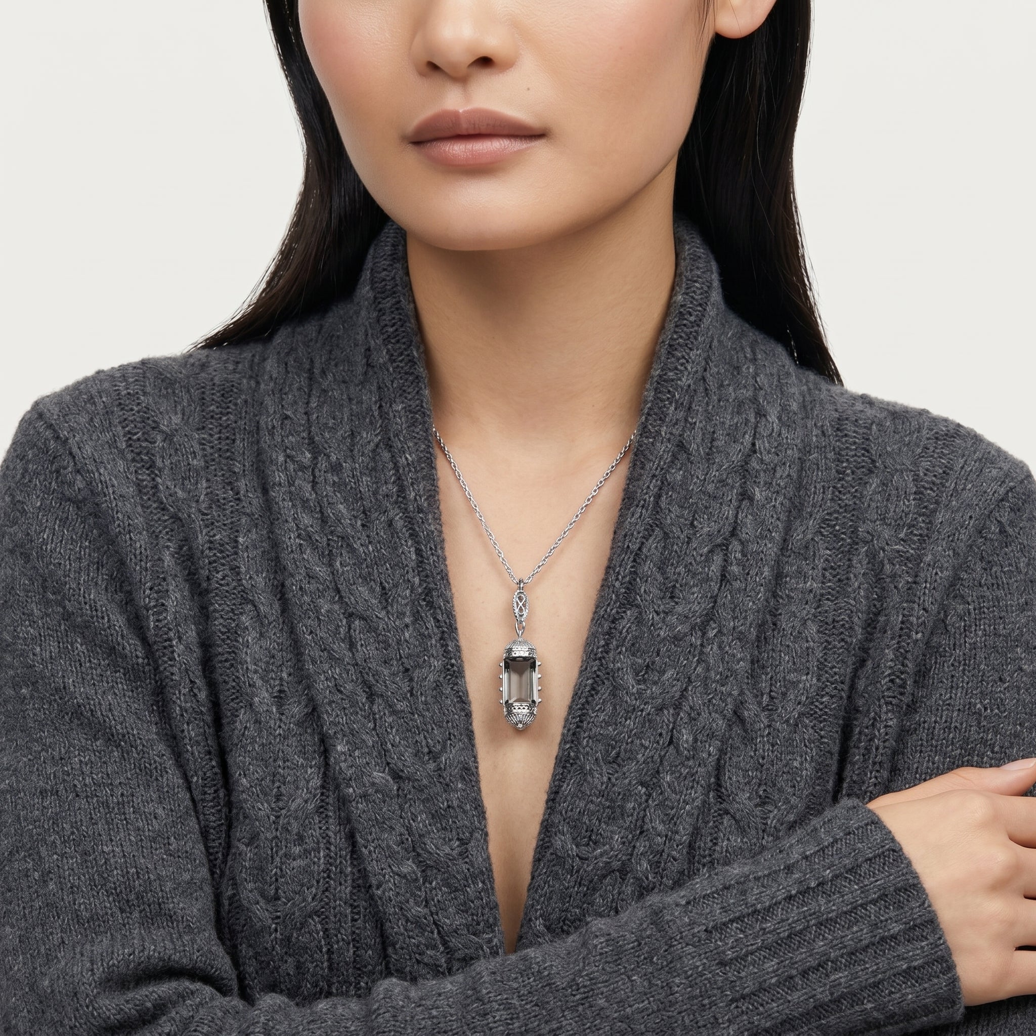Woman wearing a gray cable knit sweater with a necklace featuring a clear glass pendant.