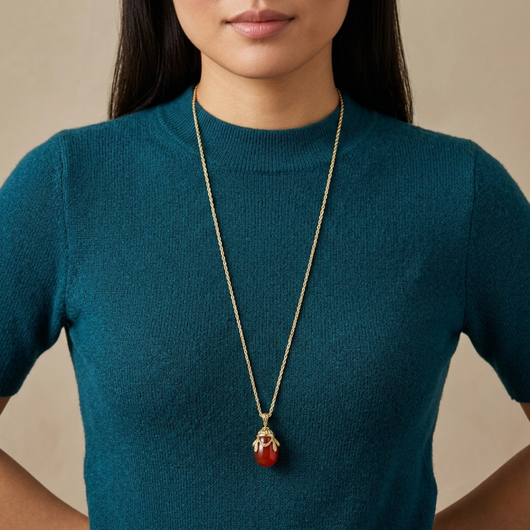 Person wearing a teal sweater with a long necklace featuring a red egg pendant.