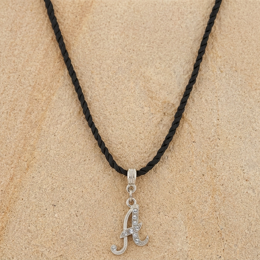 Necklace with a silver 'A' pendant on a black cord against a beige background