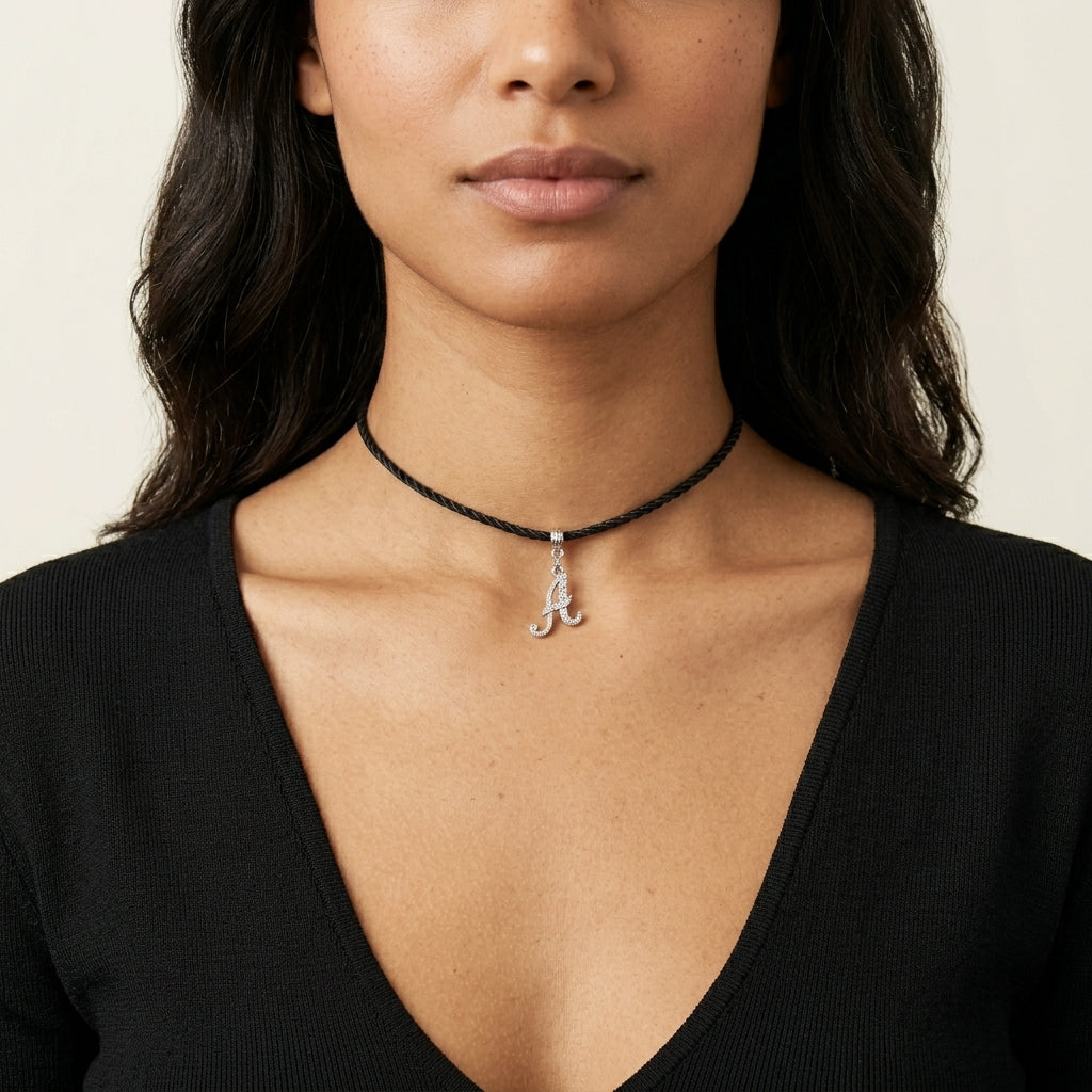 Woman in a black top wearing a black choker cord necklace with a silver tone initial pendant that has clear crystal accents