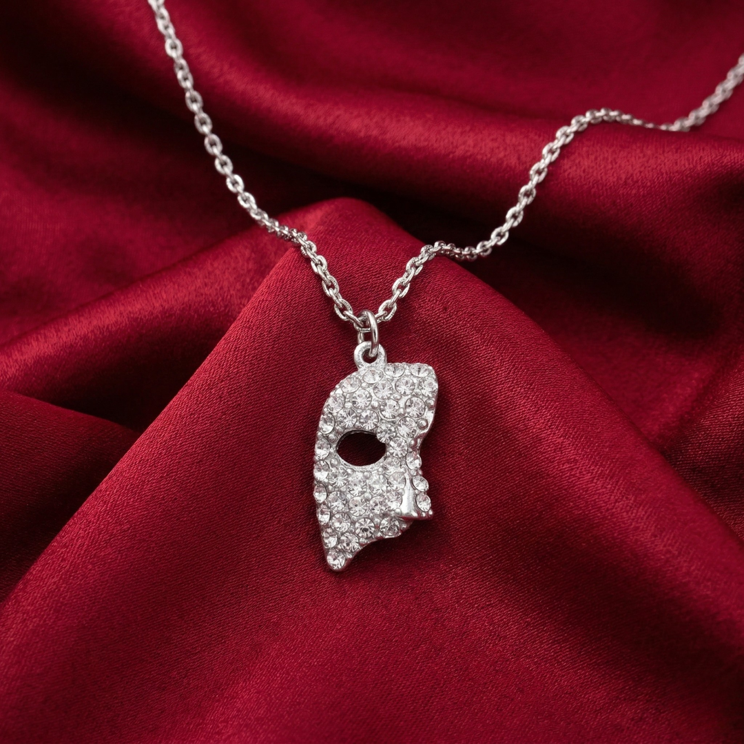 Silver necklace with a masquerade mask pendant lined filled with crystals on a red fabric background