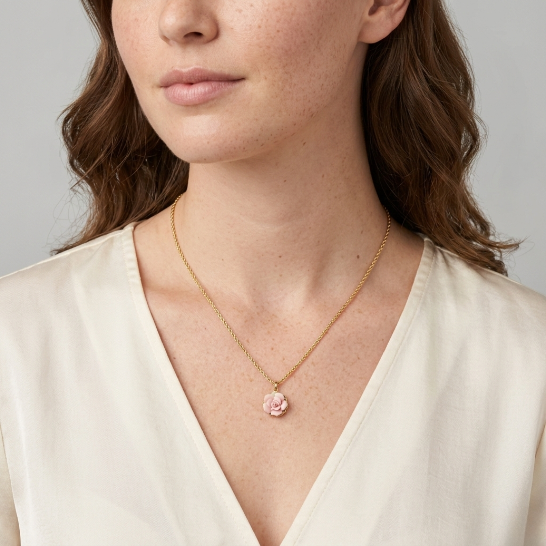 Woman wearing a gold necklace with a pink flower rose pendant against a neutral background