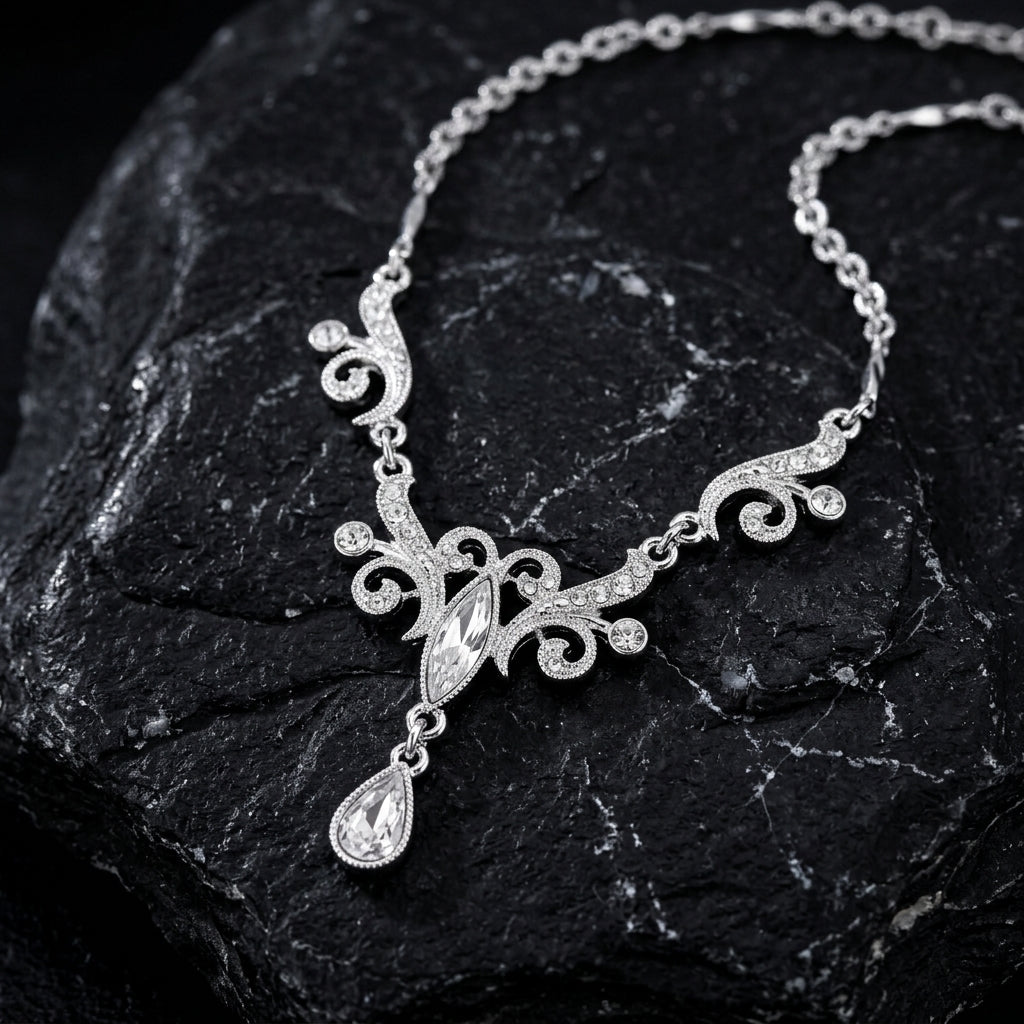 Silver tone crystal necklace with a teardrop pendant on a dark stone surface