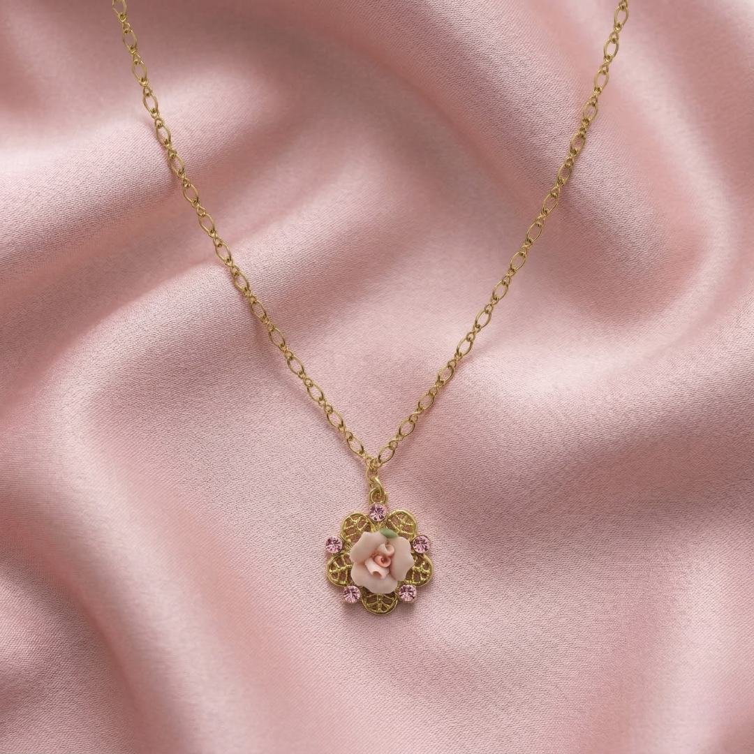 Gold necklace with a floral pink rose pendant on a pink fabric background