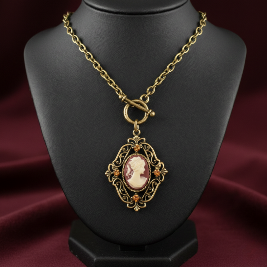 Gold necklace with a red cameo pendant on a black mannequin bust against a red fabric background.
