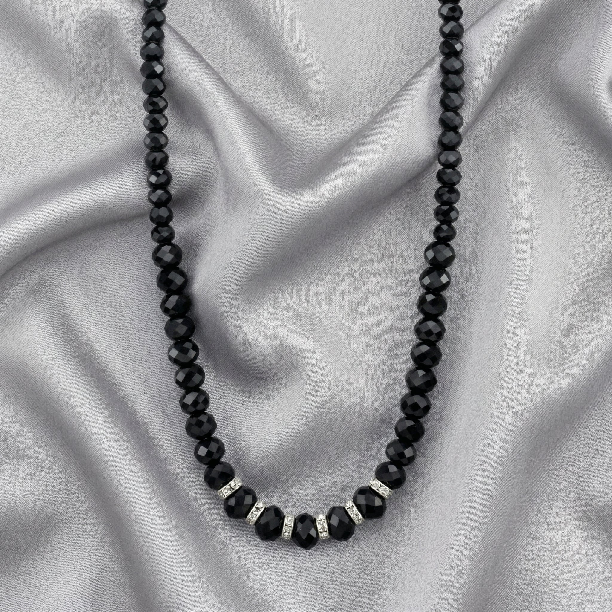 Black beaded necklace with silver accents on a gray fabric background