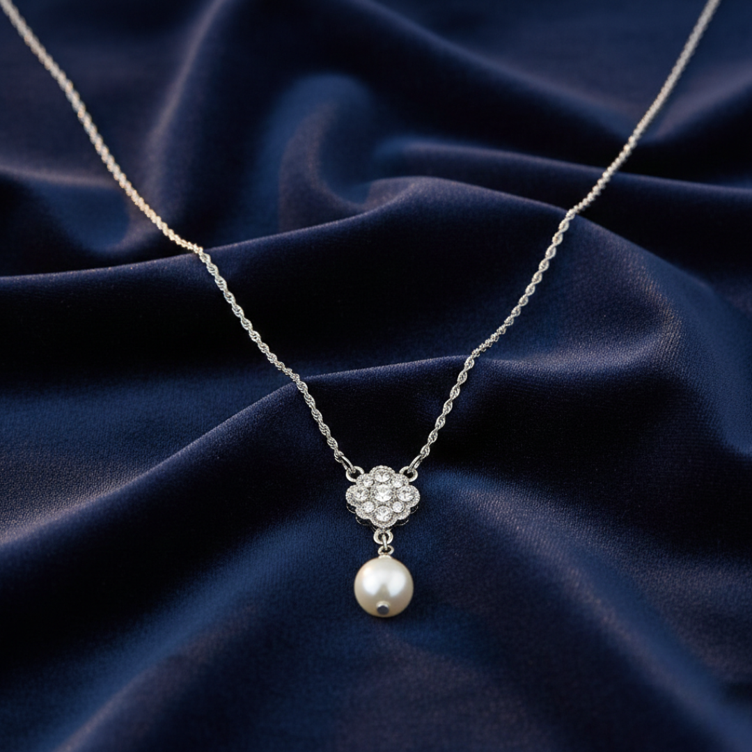 Silver necklace with a faux pearl and clear crystal pendant on a dark blue fabric background