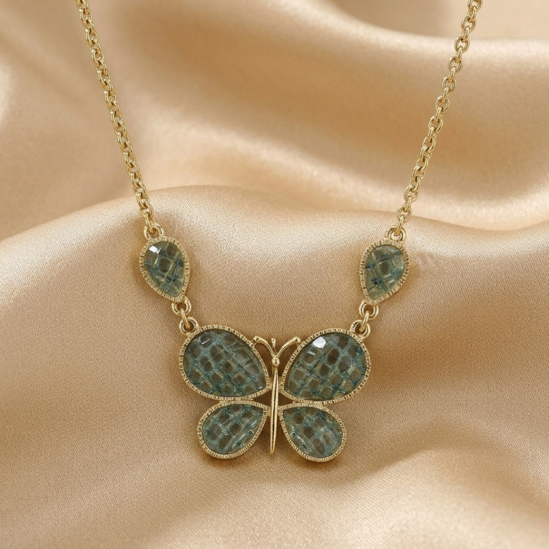 Butterfly-shaped necklace with green enamel stones on a beige fabric background